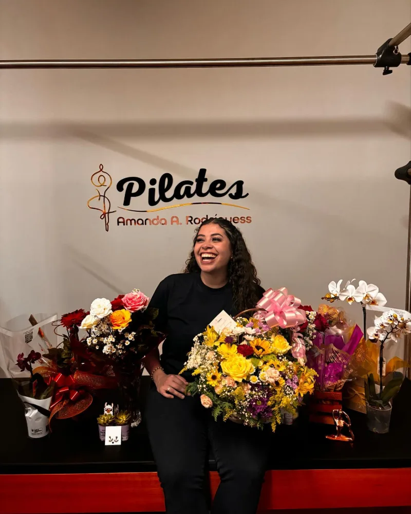 Amanda sorrindo com buquês de flores no dia da inauguração do studio, em novembro de 2024